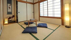 Ein traditioneller japanischer Raum mit Tatami-Boden, Shoji-Schirmwänden, einem Tatami-Tisch, Kissen und einer hängenden Leuchte.