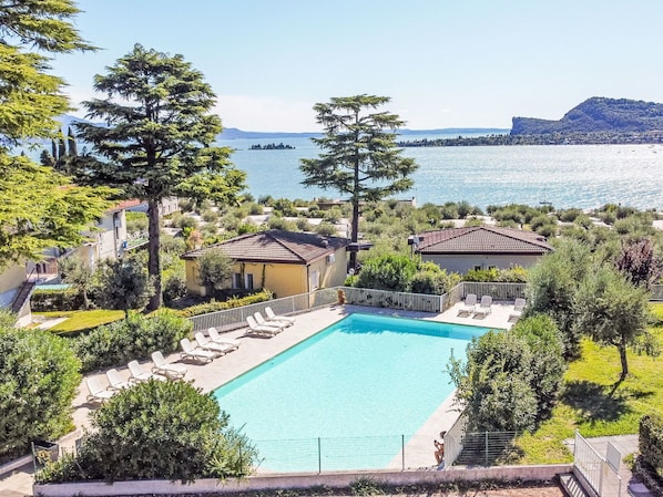 A swimming pool with lounge chairs, surrounded by greenery and overlooking a body of water with buildings in the distance.