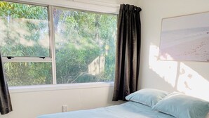 Een slaapkamer met een bed, een raam en uitzicht op groen.