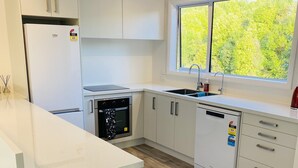 Een moderne keuken met witte kasten, een ingebouwde oven, een vaatwasser en een raam met uitzicht op groen.
