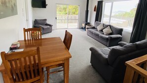Een ruime woonkamer met een houten eettafel, twee banken en een televisie aan de muur.