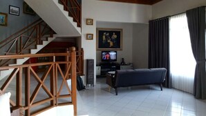 Een woonkamer met een trap, een televisie, een bank en een raam met gordijnen.