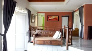 Een kamer met een houten bank, een witte deur, een foto in een lijst aan de muur en uitzicht op buiten.