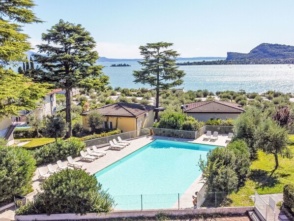 A swimming pool with lounge chairs, surrounded by greenery and overlooking a body of water with buildings in the distance.