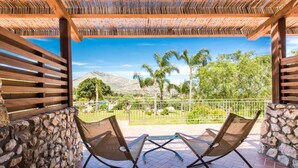 A covered patio with two mesh chairs, stone walls, and a view of palm trees and mountains.