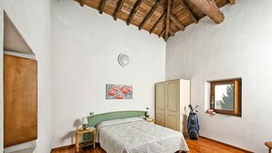 A bedroom with a wooden floor, a bed with a green headboard, a wardrobe, a window with a view, and a ceiling with wooden beams. - Nice apartment for 6 guests with WIFI, pool, A/C, TV, balcony and pets allowed (Salò)