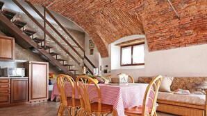 A dining area with a checkered tablecloth, wicker chairs, a brick ceiling, and a kitchen with wooden cabinets.