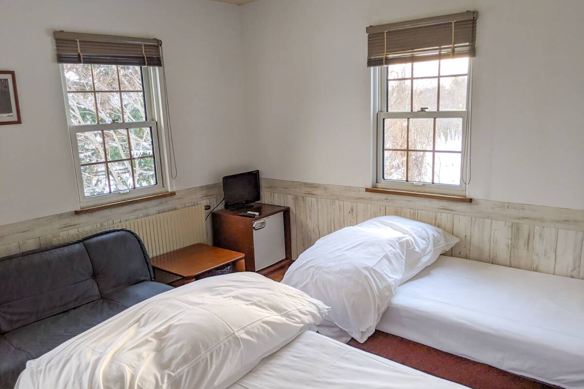 Quarto com duas camas, um sofá e uma mesa pequena com televisão.