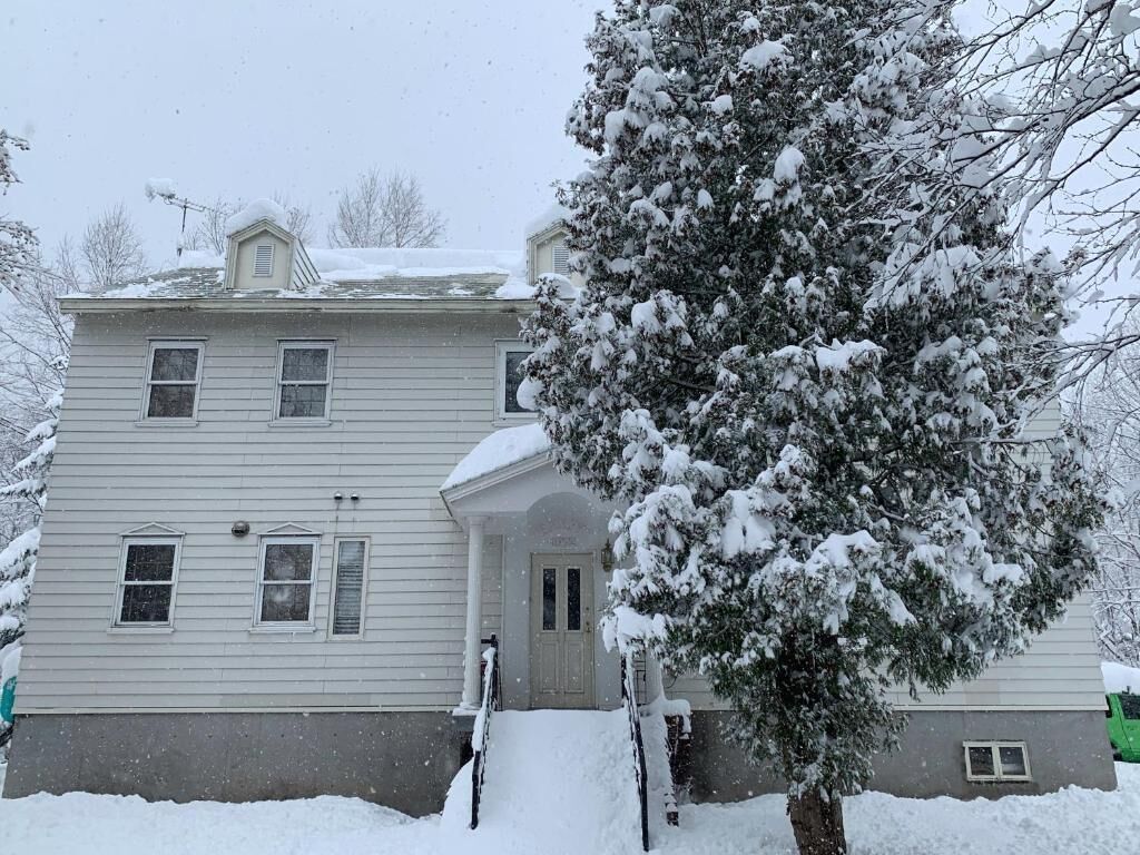 Ein zweistöckiges Haus mit einer Veranda und einem schnee bedeckten Baum.
