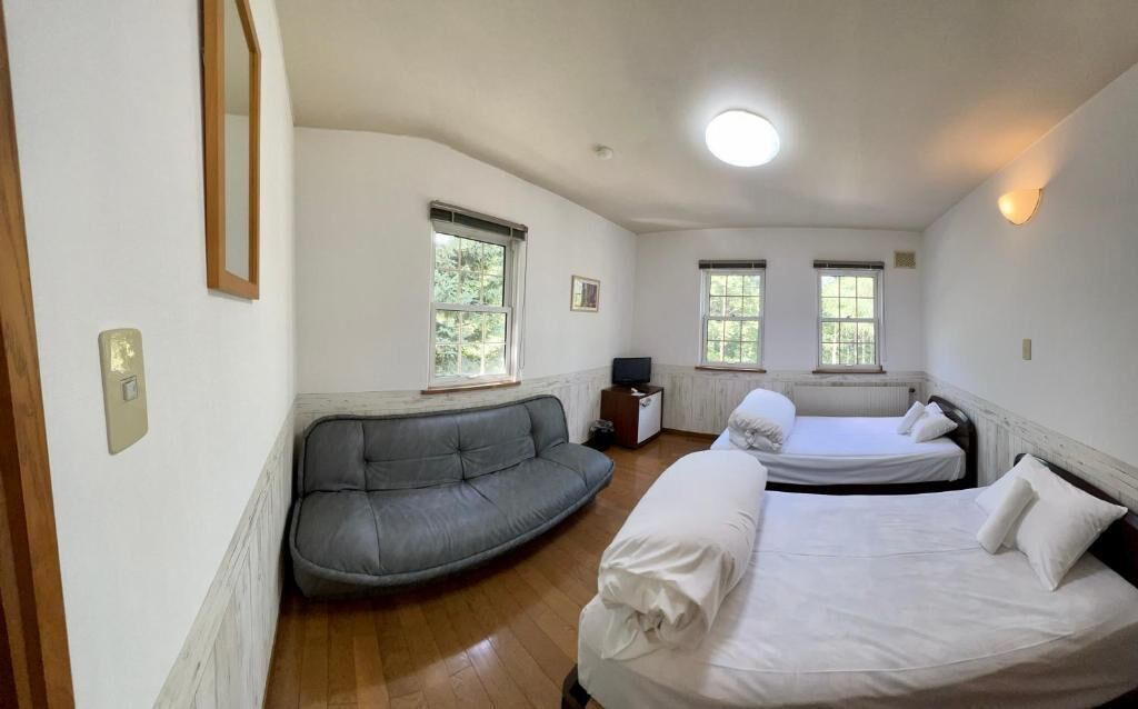 A room with a curved gray sofa, two beds, and a small table.