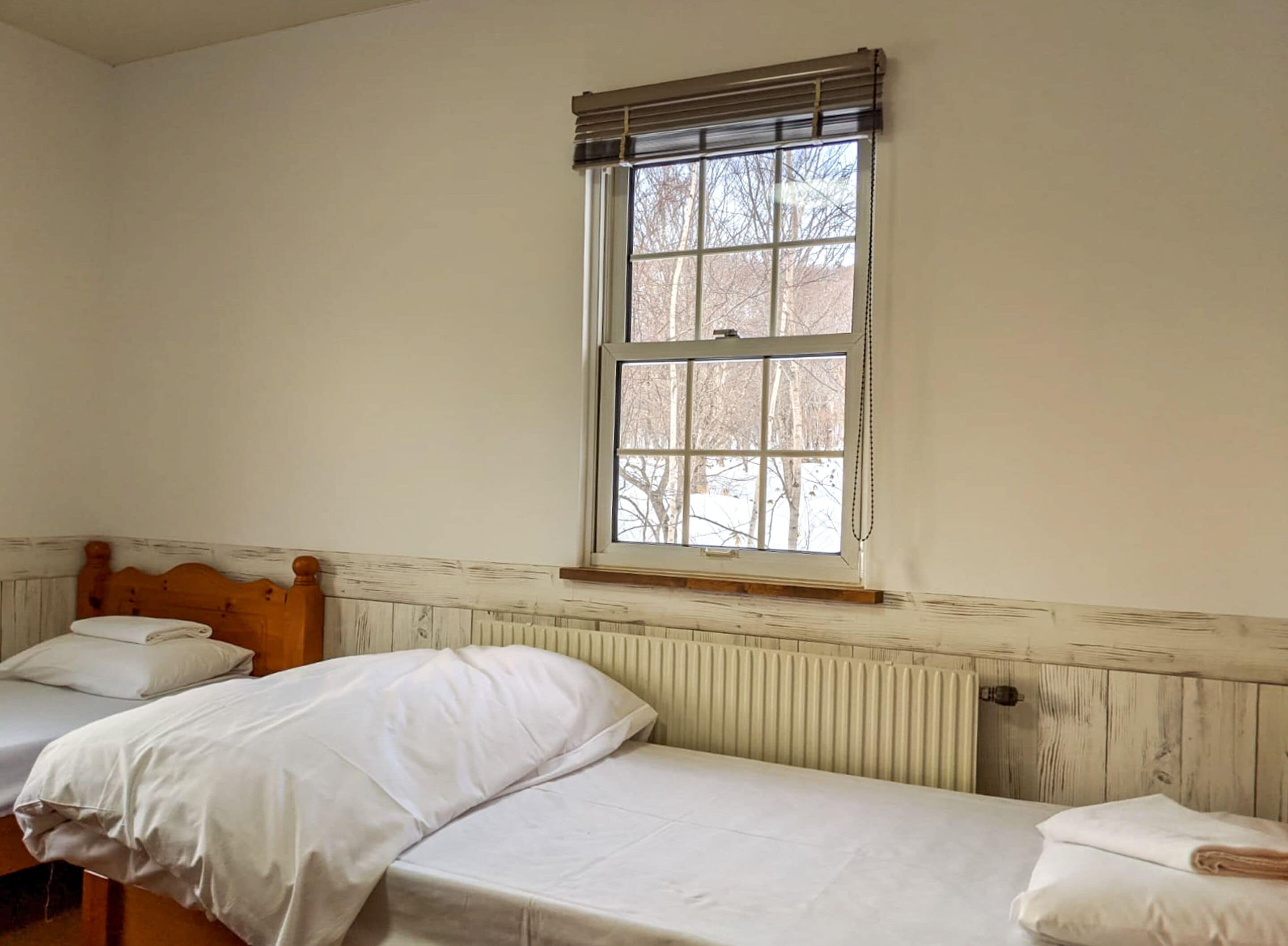 A room with two single beds, a window with blinds, and a radiator.