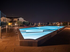 Una piscina rettangolare con superficie d'acqua blu trasparente, circondata da un percorso lastricato.