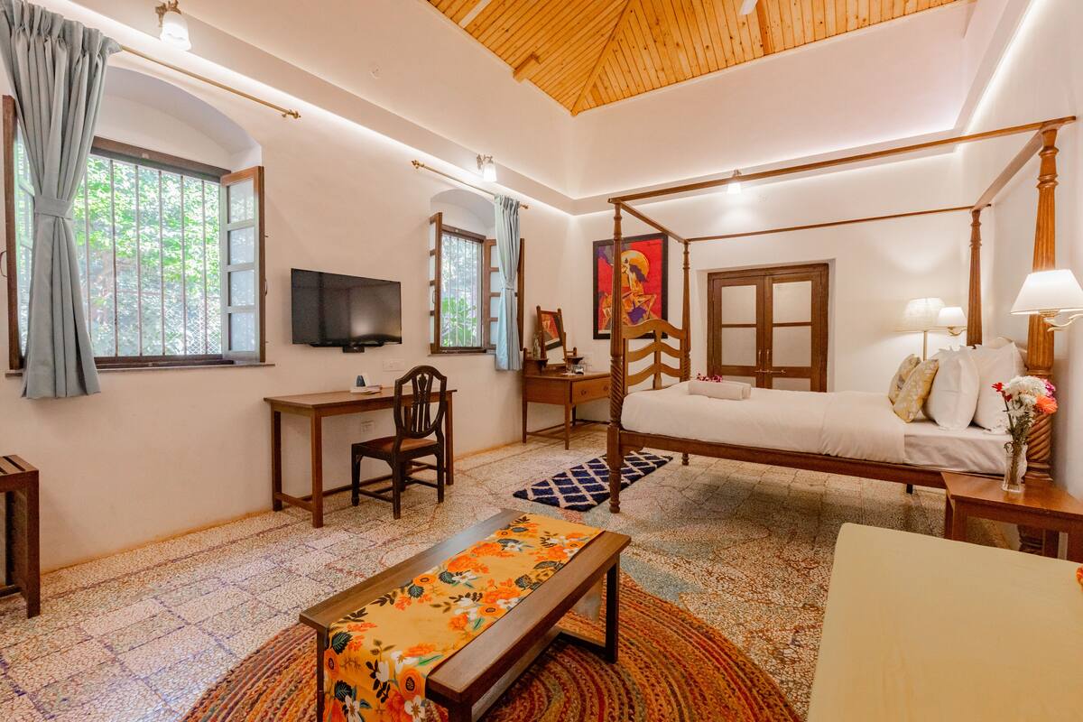 Una habitación con una cama con dosel, un escritorio con silla, un televisor y una ventana con cortinas.