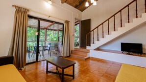 A spacious living area with a wooden staircase, a television, and a sliding glass door leading to an outdoor patio. - Radha Cottage (Karjat)