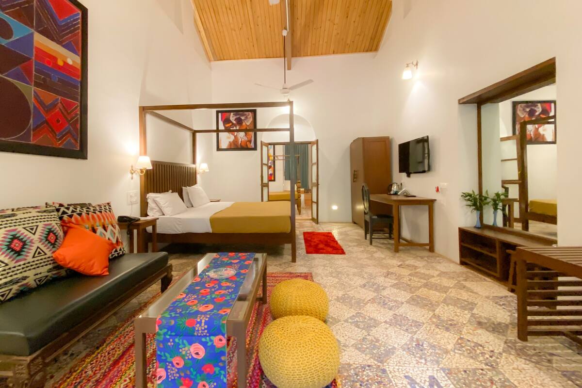 Habitación de hotel con cama, sofá, escritorio, silla, televisor y espejo.