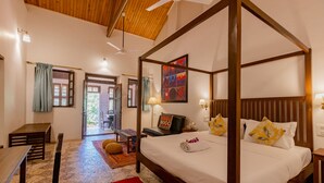 A four-poster bed with a wooden frame, a red rug, and a painting on the wall. - Radha Cottage (Karjat)