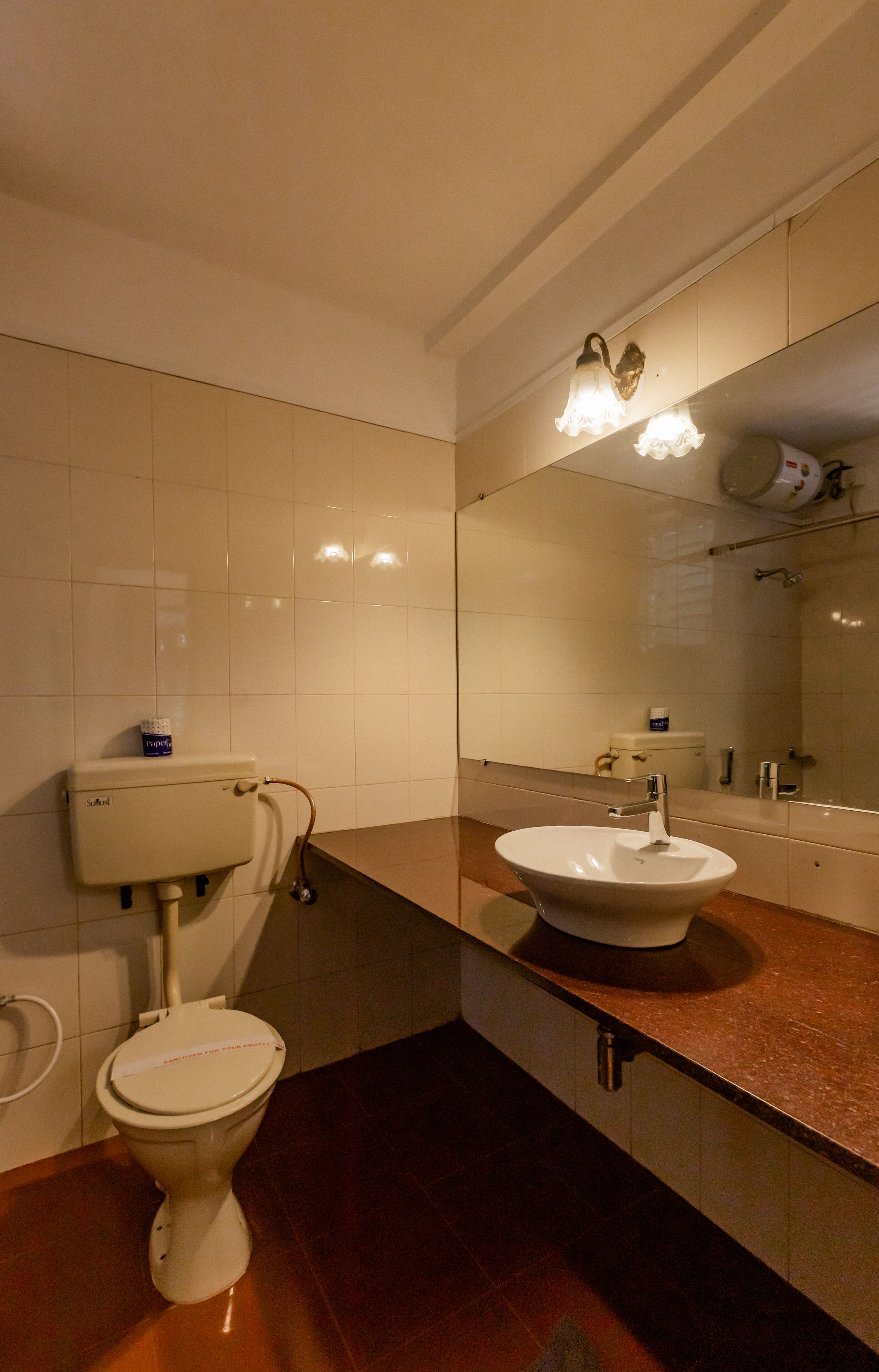 Une salle de bain équipée de toilettes, d’un lavabo, d’un miroir et de murs carrelés.
