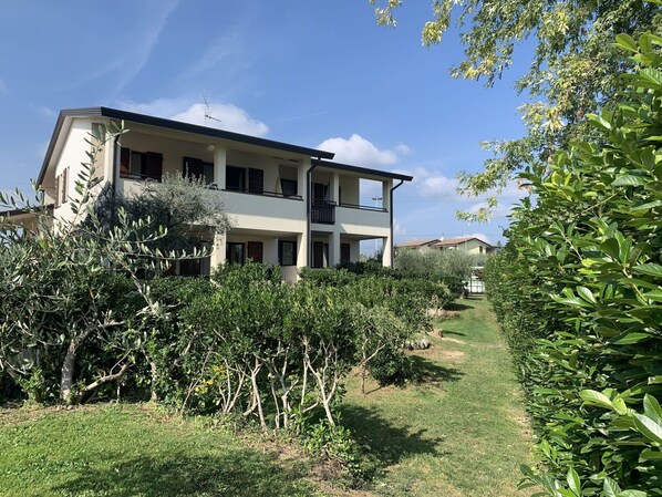A two-story building with a balcony, surrounded by lush greenery and a clear sky.