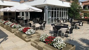 Un espace extérieur aménagé en terrasse, avec des tables et des chaises, entouré de parterres de fleurs.