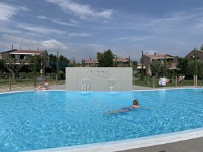 A swimming pool with a stone wall in the center, surrounded by houses and greenery.