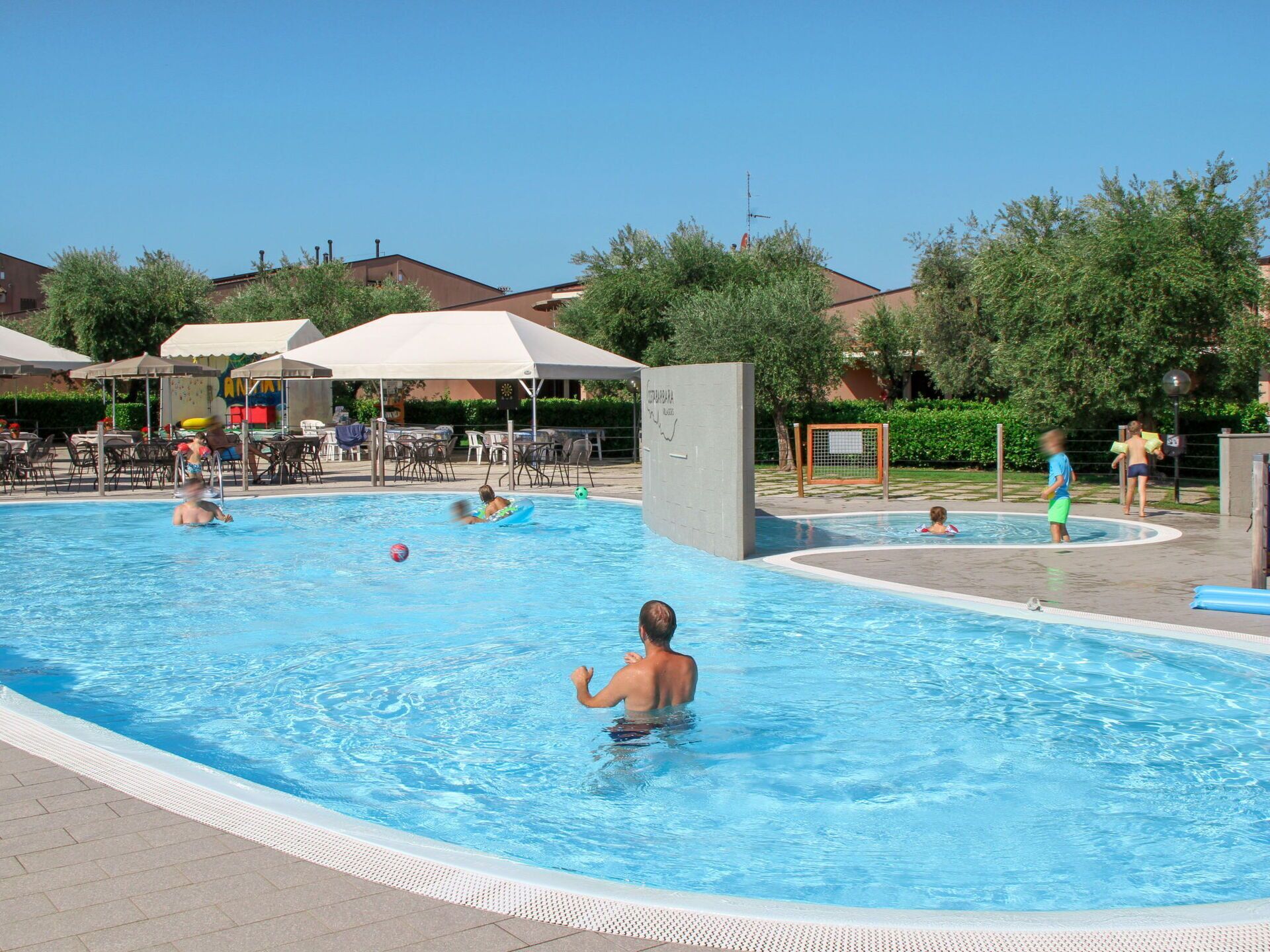A swimming pool with multiple lanes, surrounded by lounge chairs and umbrellas, and a few people swimming and playing.