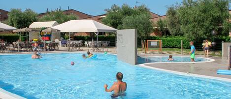 A swimming pool with multiple lanes, surrounded by lounge chairs and umbrellas, and a few people swimming and playing.