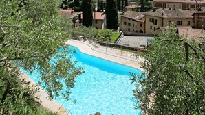 A swimming pool with clear blue water, surrounded by greenery and buildings with traditional architecture.
