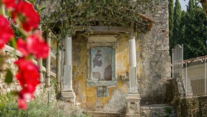Une ancienne construction en pierre, dotée d’une porte d’entrée centrale, flanquée de colonnes, et d’un petit jardin avec un chemin de gravier menant à l’entrée.
