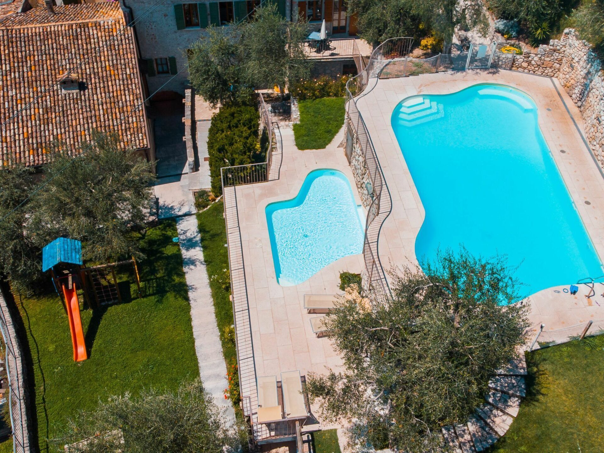 An aerial view of a residential property with a swimming pool, a patio area, and a small slide.