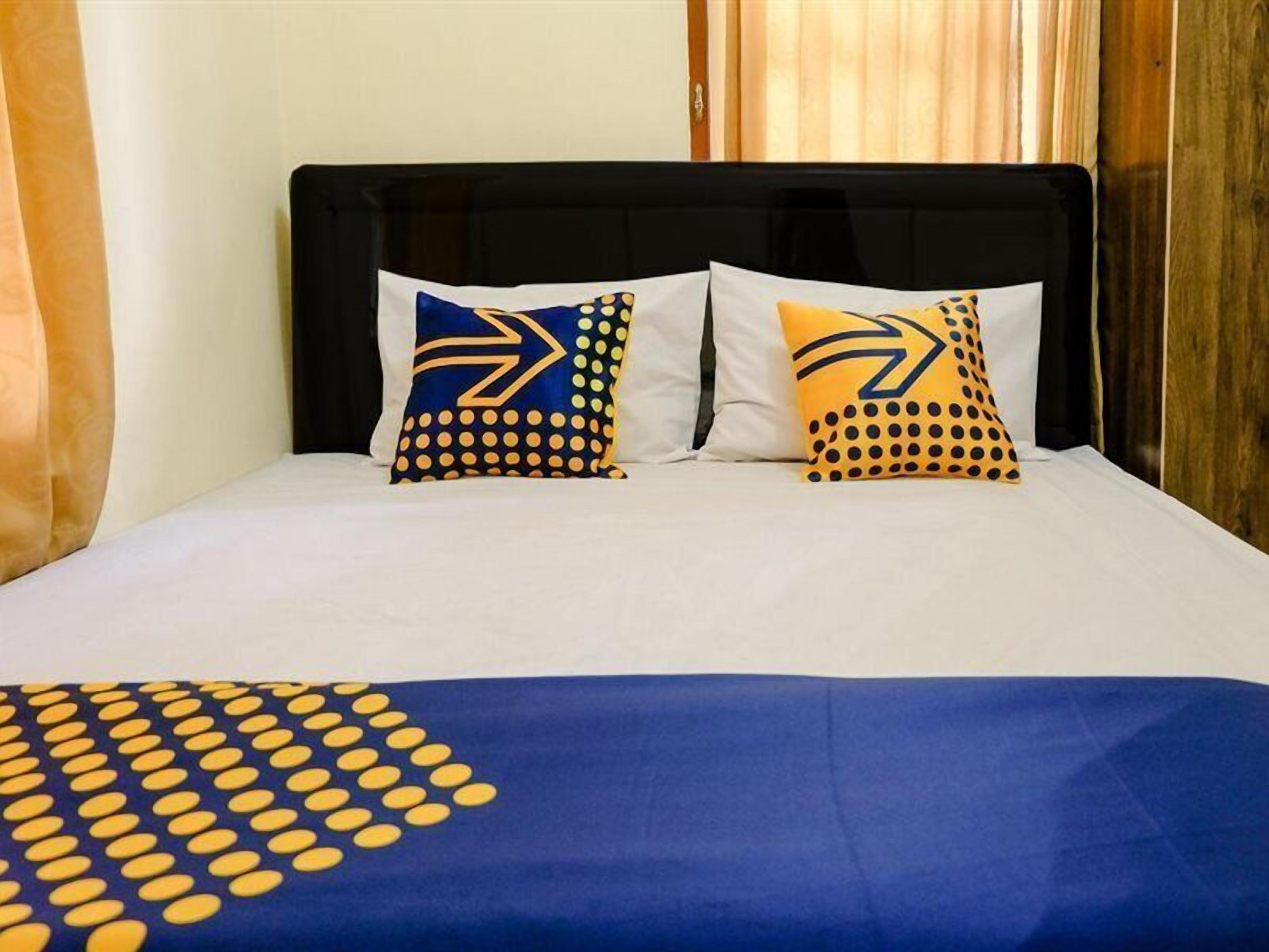 A bed with a black headboard, two pillows with a yellow and blue pattern, and a blue blanket with yellow dots.