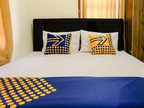 Ein Bett mit schwarzem Kopfteil, zwei Kissen mit gelb-blauen Mustern und einer blauen Decke mit gelben Punkten.