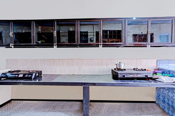 A kitchen with two gas stoves, cabinets above the counter, and a window with reflections. - Garuda Guest House (Banjarbaru)