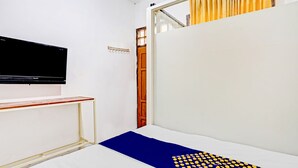 Une pièce comprenant un lit, un téléviseur fixé au mur et une porte donnant sur une autre pièce.