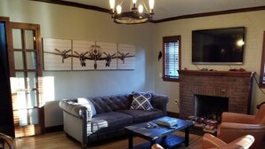 A living room with a sofa, armchairs, a coffee table, a fireplace, and a TV mounted on the wall. - Charming English Tudor (Sedalia)