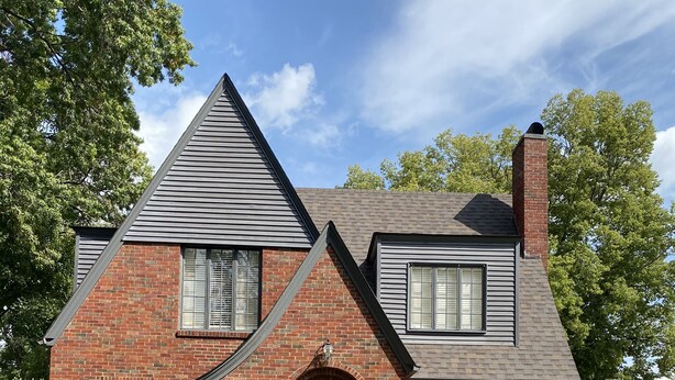 A two-story brick house with a gabled roof, a front entrance with a door and steps, and a small front yard with a lawn and a tree. - Charming English Tudor (Sedalia)