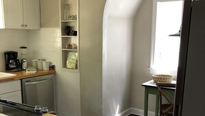 A kitchen with a wooden countertop, a built-in oven, and a coffee maker. There is a window with a basket on the windowsill and a chair. - Charming English Tudor (Sedalia)