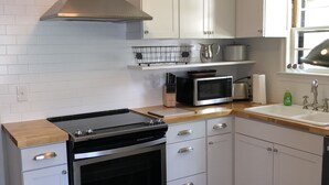 A modern kitchen with white cabinets, stainless steel appliances, and a wooden countertop. - Charming English Tudor (Sedalia)