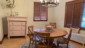 A dining room with a wooden table, four chairs, a chandelier, a vase with flowers, and a radiator. - Charming English Tudor (Sedalia)