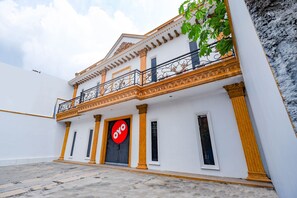 A building with a white facade, a balcony with ornate railings, and a large circular sign with the word "OYO". - OYO 2856 Wisma Fortuna Syariah (Surakarta)