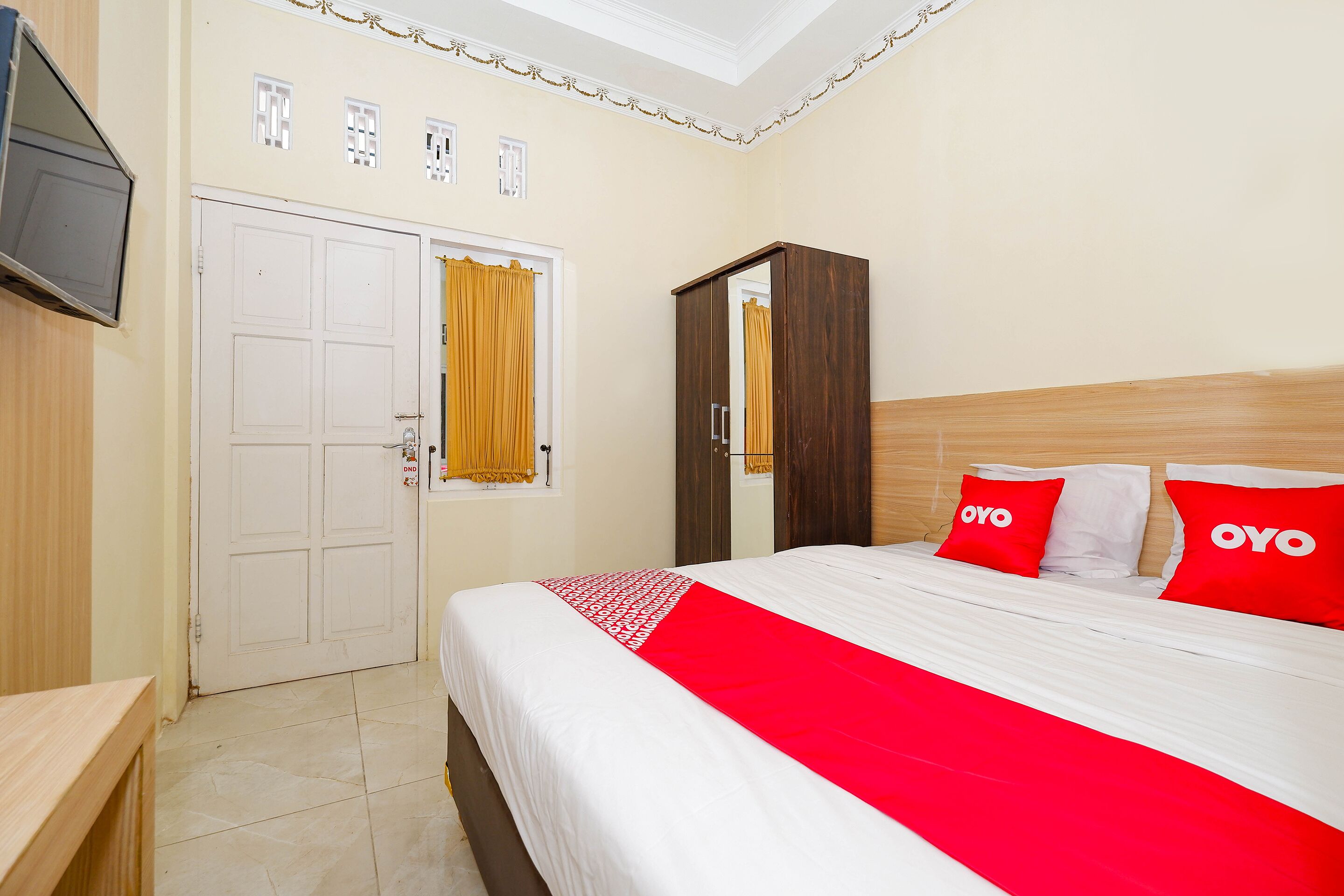 A hotel room with a bed, a wardrobe, a television, and a door with a curtain.