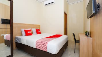 A hotel room with a bed, a desk, a chair, a TV mounted on the wall, and an air conditioning unit.