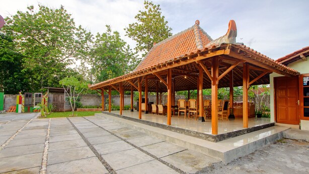 A covered outdoor seating area with a tiled roof and wooden beams, surrounded by a stone patio. - OYO 2634 Griya Birowo Syariah (Wonosari)