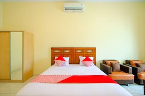 A hotel room with a bed, two armchairs, a wardrobe, and an air conditioning unit. - OYO 2634 Griya Birowo Syariah (Wonosari)
