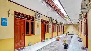 A corridor with tiled flooring, potted plants, and multiple doors with air conditioning units. - OYO Life 2546 Griya Widya Syariah (Klaten)