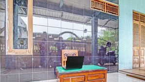 A room with a tiled floor, a wooden table with a laptop, and a large window with a view of the outside. - OYO Life 2546 Griya Widya Syariah (Klaten)
