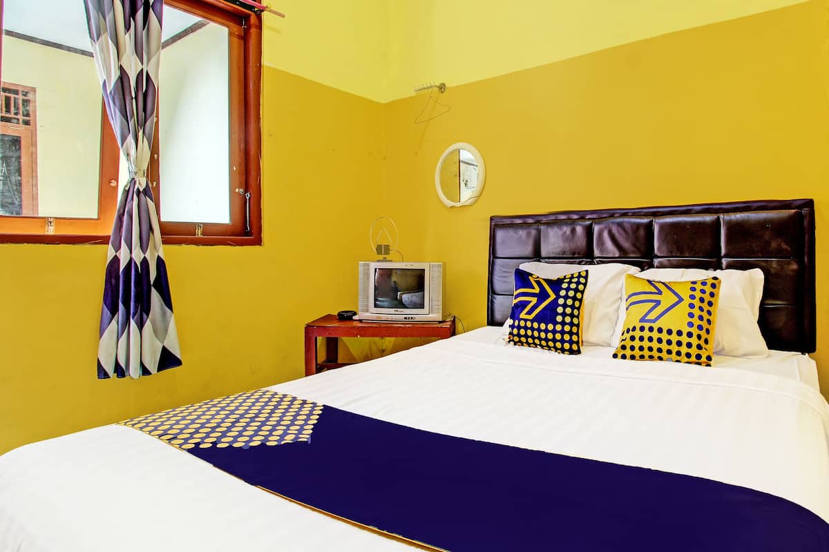 Une chambre avec un lit, un téléviseur posé sur une table de chevet et une fenêtre avec des rideaux.