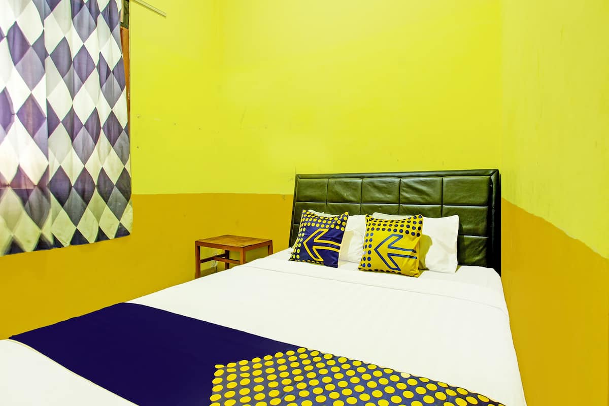 Un lit recouvert d’une couvre-lit à motifs blancs et bleus, doté d’une tête de lit rembourrée de couleur verte et de deux oreillers à motifs géométriques.