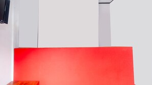 A room with a red accent wall, a wooden bench, and a flat-screen TV mounted on the wall. - OYO 2471 Swarna Raya (Bayah)