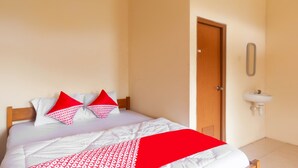 A neatly made bed with a white and red patterned bedspread, two red pillows, and a wooden headboard. A white air conditioning unit is mounted on the wall above the bed. - OYO 2471 Swarna Raya (Bayah)