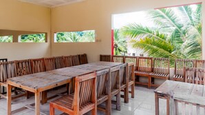 A spacious room with a long wooden table and benches, large windows with tropical views, and a tiled floor. - OYO 2471 Swarna Raya (Bayah)